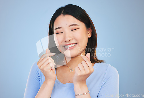 Image of Happy asian woman, hands and love sign or gesture in romance against a blue studio background. Face of calm female person smile in happiness with loving emoji, icon or symbol for valentines day