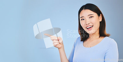 Image of Asian woman, point and studio portrait with space, mockup and happy for promotion by blue background. Japanese student, girl and smile for review, opinion or feedback with choice, decision and sign