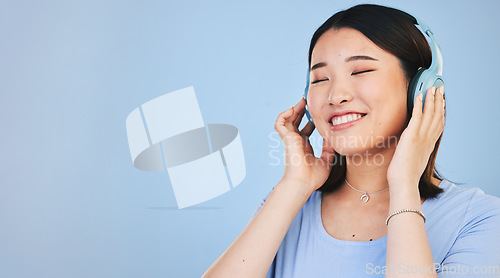 Image of Face of happy Asian woman in studio with headphones for streaming radio, subscription and relax. Sound, smile and person listen to music, audio and track for calm on mockup space on blue background