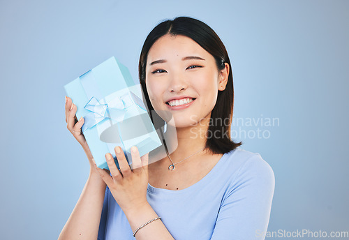 Image of Happy, Asian woman and portrait with a gift, box and present on blue background in studio with promotion or discount. Model, smile and face with happiness for giving or receiving surprise package