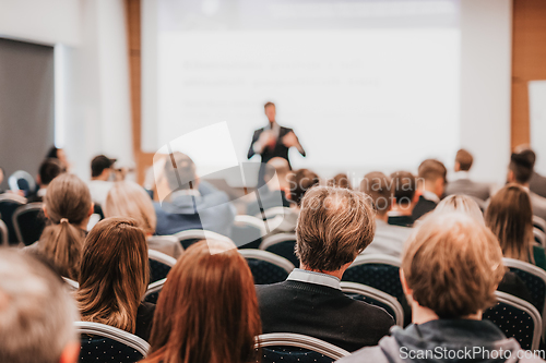 Image of Speaker giving a talk in conference hall at business event. Rear view of unrecognizable people in audience at the conference hall. Business and entrepreneurship concept.