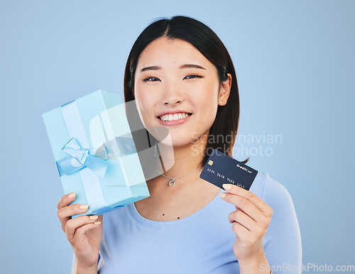 Image of Woman, credit card and gift box, prize or retail giveaway and payment in portrait and a blue background. Happy Asian person or winner for present, finance bonus and shopping sale or success in studio