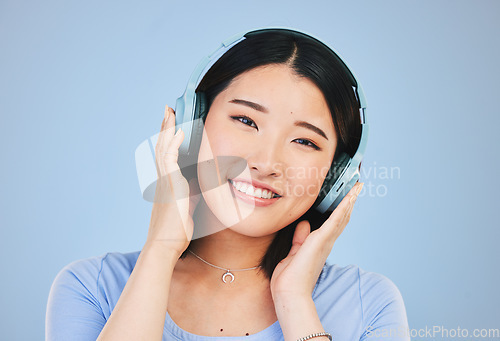 Image of Portrait of happy Asian woman in studio with headphones for streaming radio, subscription and relax. Sound, podcast and face of person listening to music, audio and track for calm on blue background