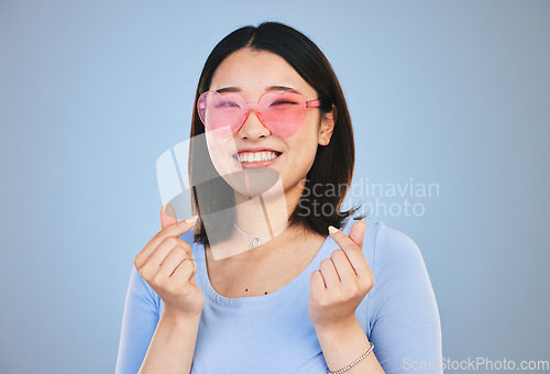 Image of Happy asian woman, portrait and sunglasses with love hands, sign or gesture against a blue studio background. Female person smile in happiness with loving emoji, icon or symbol for valentines day