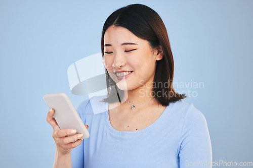 Image of Happy asian woman, phone and typing in social media, networking or communication against a blue studio background. Female person smile in online research, chatting or texting on mobile smartphone app