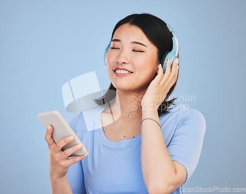 Image of Music, headphones and happy Asian woman with phone for streaming radio, subscription and relax. Sound, online podcast and face of person listening to song, audio and track for calm on blue background