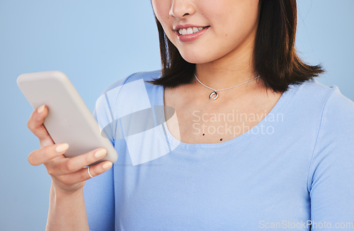 Image of Woman, phone and hand with texting, studio or chat for networking, smile or app by blue background. Student, girl and smartphone for post, mobile connection and social media for typing, press or web