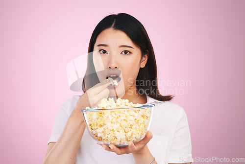 Image of Popcorn, hungry and woman portrait eating a movie snack in a studio with watching tv and food. Pink background, Asian female person and surprise with chips in a glass bowl with film and series