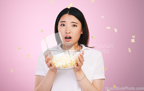 Image of Surprise, woman and portrait with horror and popcorn, bowl or food for watching tv, movies or shock for announcement. Wow, face and scared Asian model on pink background in studio with film snack