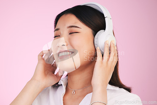 Image of Headphones, happy and young woman in a studio listening to music, playlist or album for entertainment. Smile, calm and Asian female model streaming a song or radio isolated by a pink background.