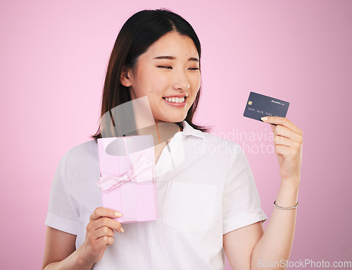 Image of Credit card, gift box and young woman in a studio online shopping a sale, discount or deal. Happy, smile and Asian female model buying a present with retail promotion isolated by a pink background.