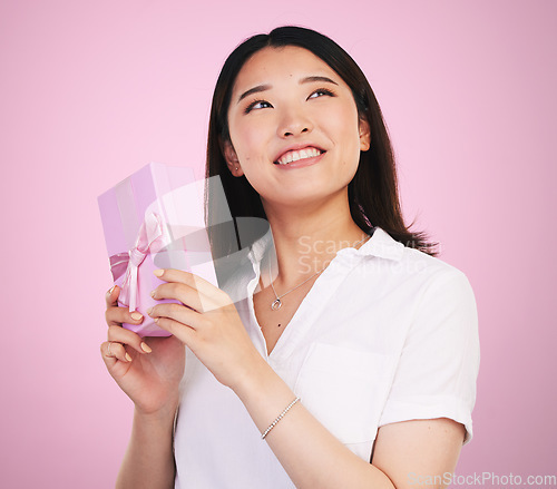 Image of Gift, thinking and Asian woman giving present box happy for celebration isolated in a studio pink background. Giveaway, ribbon and person with happiness for surprise or prize package with smile