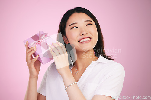 Image of Woman, gift box and thinking in studio of birthday, surprise and happiness on face for celebration in pink background. Present, package and curious Asian model with a guess for giveaway or promotion