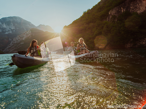 Image of A group of friends enjoying fun and kayaking exploring the calm river, surrounding forest and large natural river canyons during an idyllic sunset.