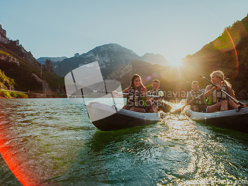 Image of A group of friends enjoying fun and kayaking exploring the calm river, surrounding forest and large natural river canyons during an idyllic sunset.