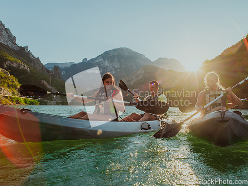 Image of A group of friends enjoying fun and kayaking exploring the calm river, surrounding forest and large natural river canyons during an idyllic sunset.