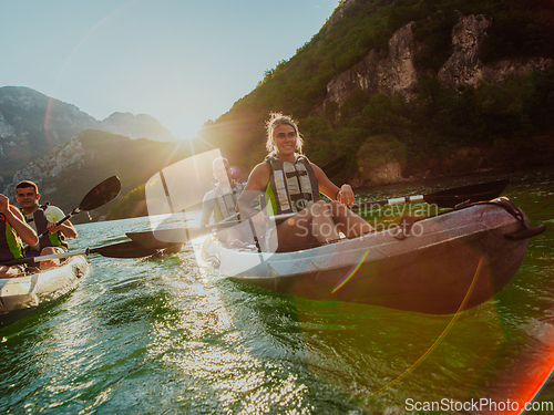 Image of A group of friends enjoying fun and kayaking exploring the calm river, surrounding forest and large natural river canyons during an idyllic sunset.