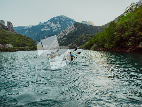 Image of A group of friends enjoying fun and kayaking exploring the calm river, surrounding forest and large natural river canyons during an idyllic sunset.