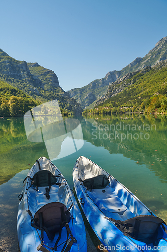 Image of An idyllic photo of two kayaks on the river bank. In the background of green forest area and mountains