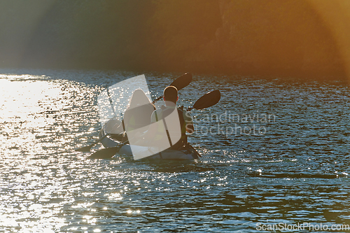 Image of A young couple enjoying an idyllic kayak ride in the middle of a beautiful river surrounded by forest greenery in sunset time