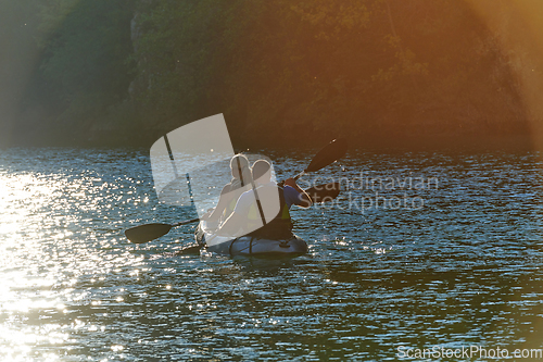 Image of A young couple enjoying an idyllic kayak ride in the middle of a beautiful river surrounded by forest greenery in sunset time