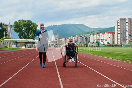 Image of A Muslim woman in a burqa running together with a woman in a wheelchair on the marathon course, preparing for future competitions.