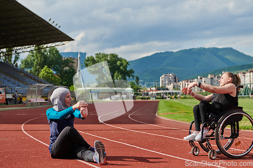 Image of Two strong and inspiring women, one a Muslim wearing a burka and the other in a wheelchair stretching and preparing their bodies for a marathon race on the track