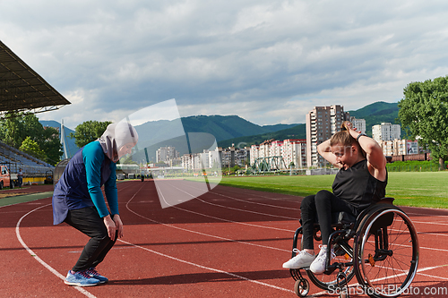 Image of Two strong and inspiring women, one a Muslim wearing a burka and the other in a wheelchair stretching and preparing their bodies for a marathon race on the track