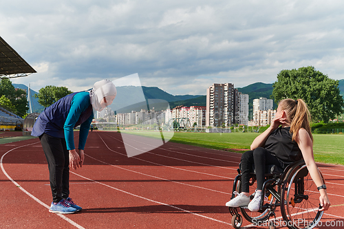 Image of Two strong and inspiring women, one a Muslim wearing a burka and the other in a wheelchair stretching and preparing their bodies for a marathon race on the track