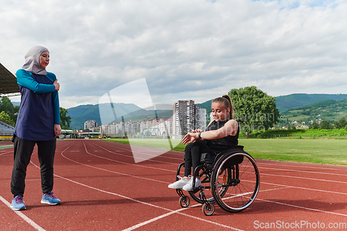 Image of A Muslim woman wearing a burqa supports her friend with disability in a wheelchair as they train together on a marathon course.