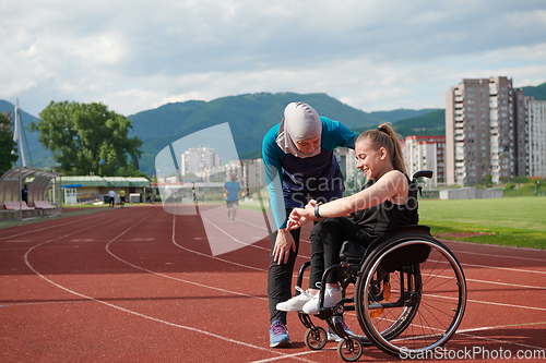 Image of A Muslim woman wearing a burqa supports her friend with disability in a wheelchair as they train together on a marathon course.