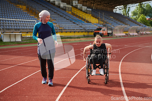 Image of A Muslim woman in a burqa running together with a woman in a wheelchair on the marathon course, preparing for future competitions.