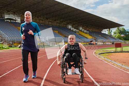 Image of A Muslim woman in a burqa running together with a woman in a wheelchair on the marathon course, preparing for future competitions.