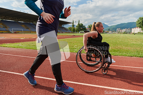 Image of A Muslim woman in a burqa running together with a woman in a wheelchair on the marathon course, preparing for future competitions.