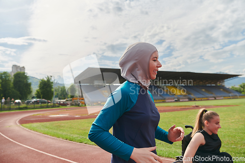 Image of A Muslim woman in a burqa running together with a woman in a wheelchair on the marathon course, preparing for future competitions.