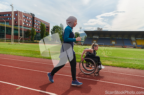 Image of A Muslim woman in a burqa running together with a woman in a wheelchair on the marathon course, preparing for future competitions.