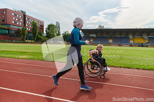 Image of A Muslim woman in a burqa running together with a woman in a wheelchair on the marathon course, preparing for future competitions.