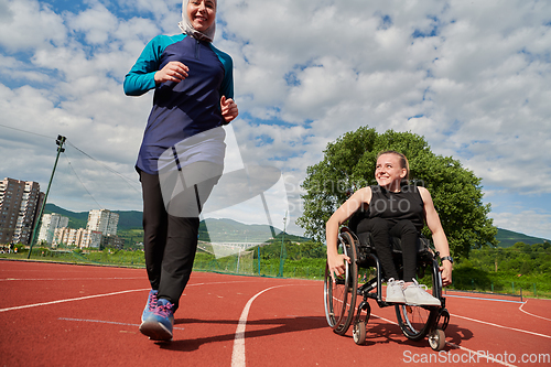 Image of A Muslim woman in a burqa running together with a woman in a wheelchair on the marathon course, preparing for future competitions.