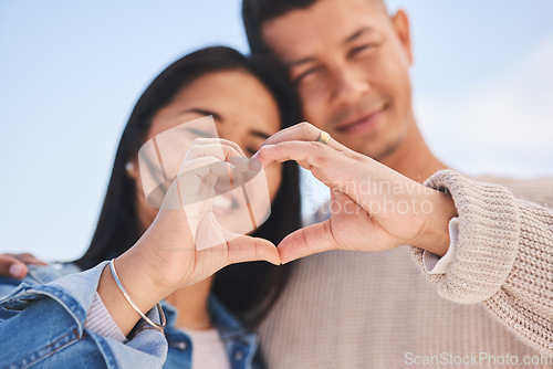 Image of Love, heart hands and portrait of happy couple with blue sky, nature and holiday travel for summer. Care, marriage and smile, loving sign language emoji with man and woman on beach vacation together.