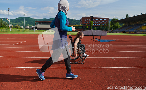 Image of A Muslim woman in a burqa running together with a woman in a wheelchair on the marathon course, preparing for future competitions.