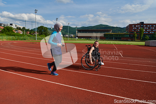 Image of A Muslim woman in a burqa running together with a woman in a wheelchair on the marathon course, preparing for future competitions.