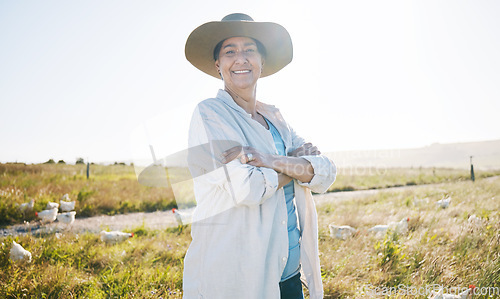 Image of Farmer, mature woman and agriculture, arms crossed on field and sustainability, land and livestock. Chicken farm, agro business and confidence, countryside and environment with nature and portrait