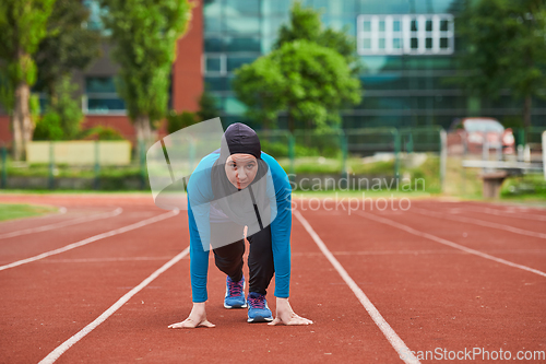 Image of Muslim woman in burqa in sporty Muslim clothes in starting pose for running