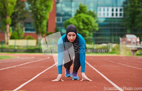 Image of Muslim woman in burqa in sporty Muslim clothes in starting pose for running