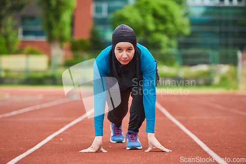 Image of Muslim woman in burqa in sporty Muslim clothes in starting pose for running