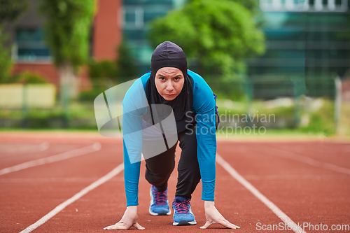 Image of Muslim woman in burqa in sporty Muslim clothes in starting pose for running