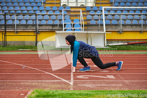 Image of Muslim woman in burqa in sporty Muslim clothes in starting pose for running