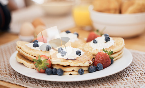 Image of Pancakes, breakfast and fruits on table in home in the morning for protein. Bread waffle, cream and food for eating, healthy diet and strawberry in wellness nutrition, blueberry and egg meal on plate