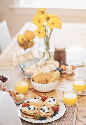 Image of Pancakes, breakfast and orange juice on table in home in the morning. Bread waffle, hands and fruits for eating, healthy diet and strawberry cream in wellness nutrition, blueberry food and egg meal.