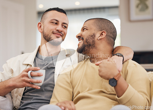 Image of Happy, love and gay couple relaxing on a sofa with a cup of coffee in the living room together. Smile, bonding and young lgbtq men with a latte sitting in the living room of their modern apartment.